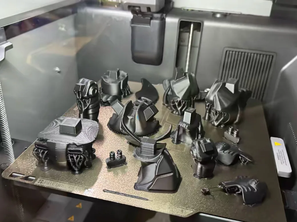 How to Make Money With a 3D Printer: The Honest Numbers (2026) 5 A full Bambu Lab print bed packed with a batch of black 3D printed model parts, showing volume production