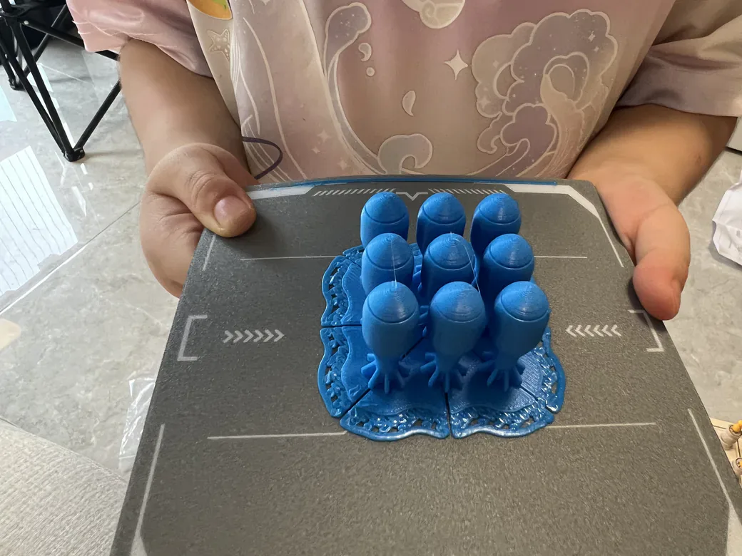 Child holding the Funbox build plate covered in blue printed spring-launcher parts
