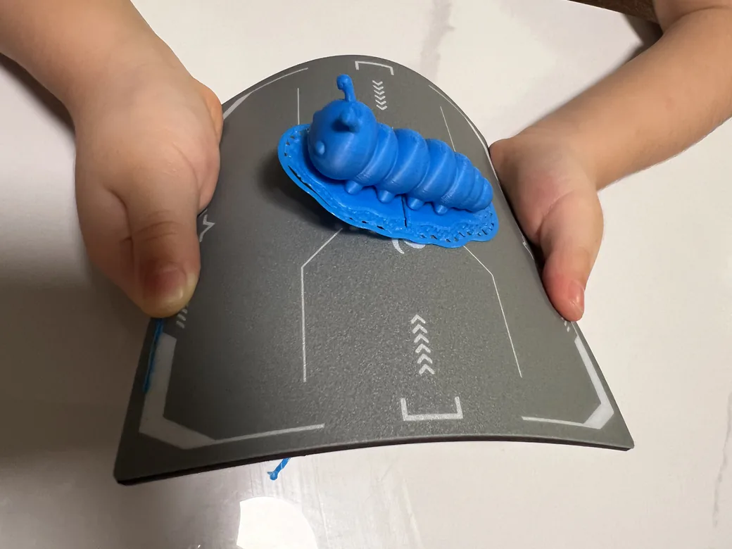 ugee Funbox 3D Printer Review: I Gave It to a 6-Year-Old for a Week 25 Child's hands flexing the magnetic plate to pop a blue printed part free