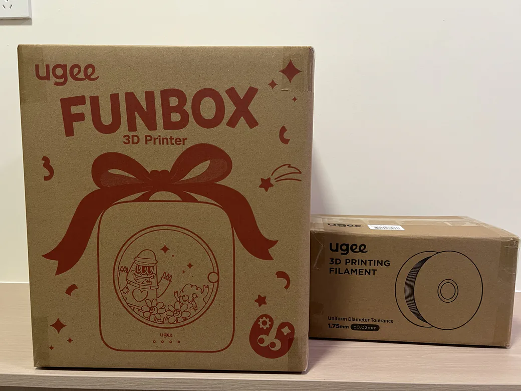 ugee Funbox 3D Printer Review: I Gave It to a 6-Year-Old for a Week 5 ugee Funbox retail box printed with a red gift bow next to a filament box