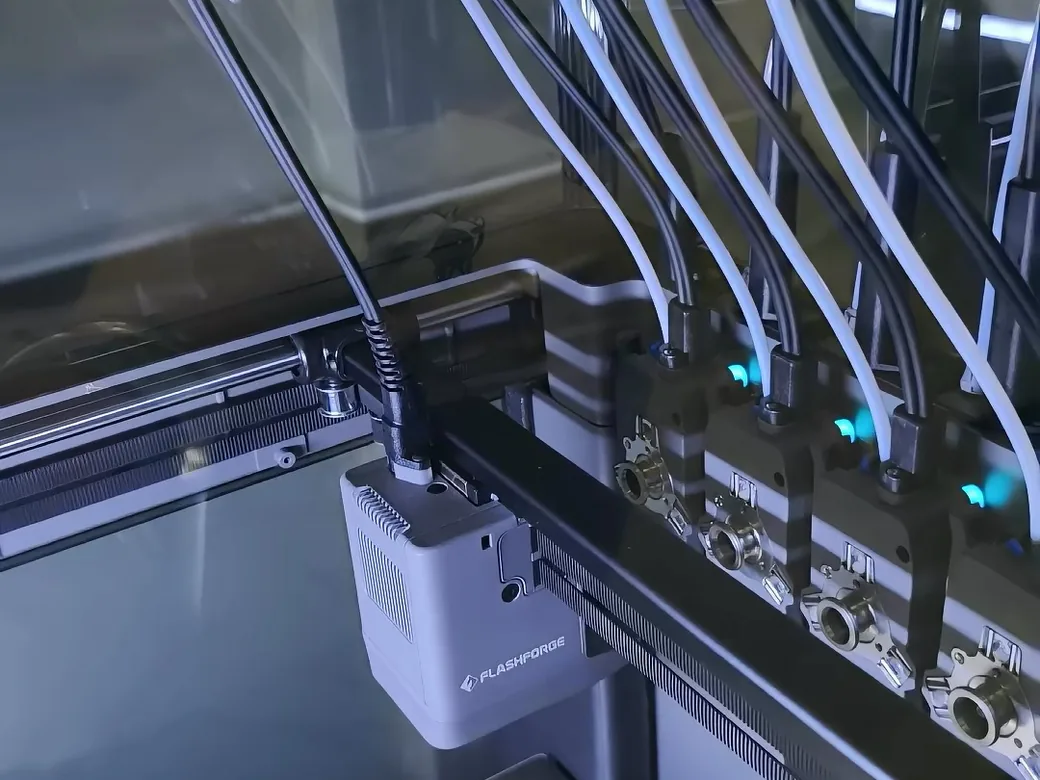 Flashforge Creator 5 carriage beside four docked toolheads lit blue, showing the FlashSwap coupling system