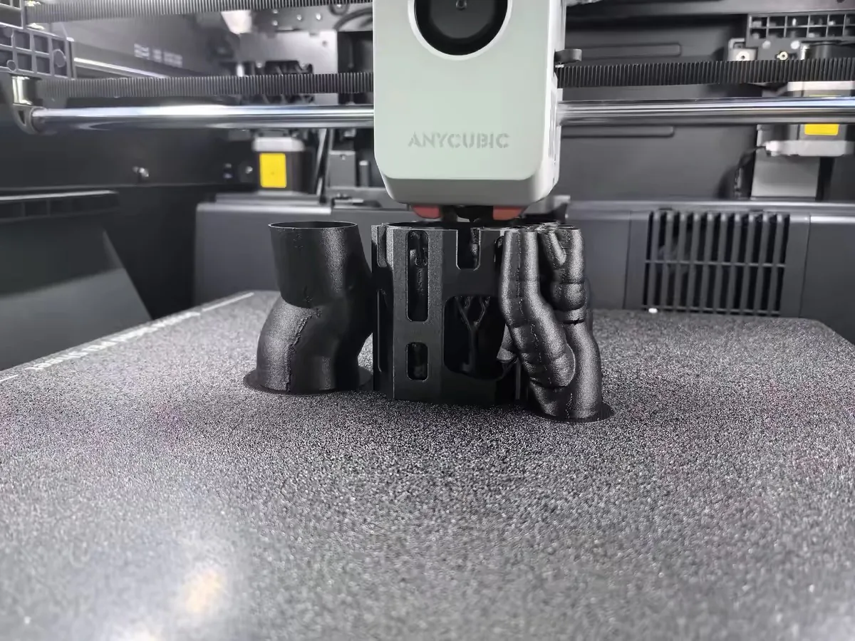 Anycubic Kobra S1 Max vs Creality K2 Plus: Same Promises, Different Failure Modes 4 The Anycubic Kobra S1 Max print head laying down black organic-shaped parts on the textured build plate
