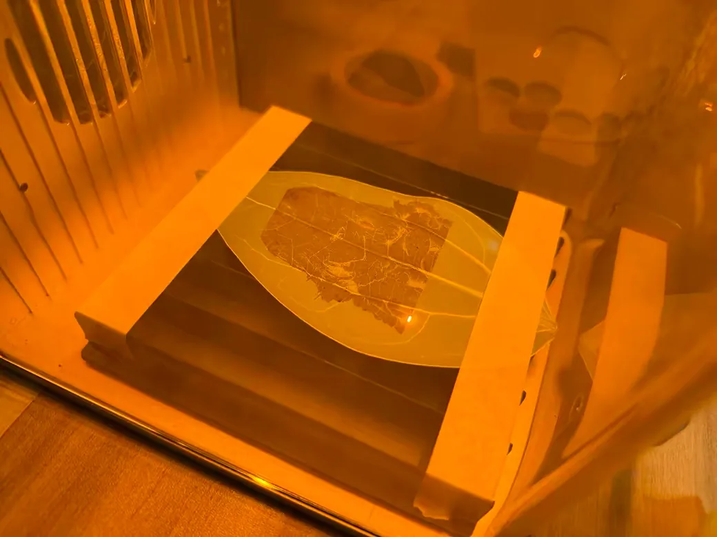 A wood piece being laser engraved inside the xTool F2's chamber, viewed through the amber safety window
