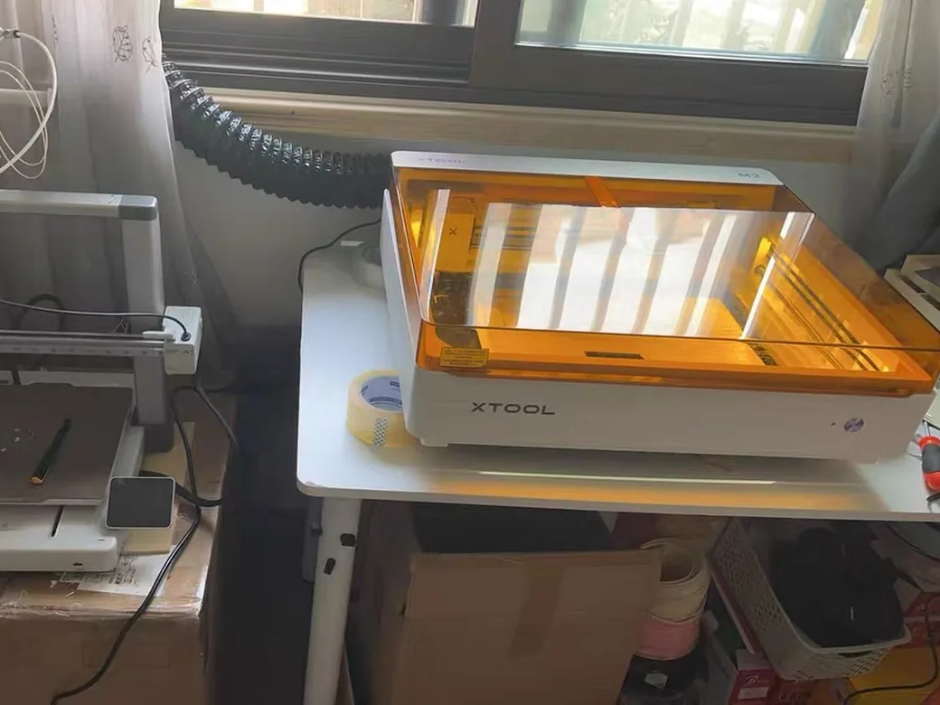xTool M2 enclosed laser connected to an exhaust hose routed toward a window