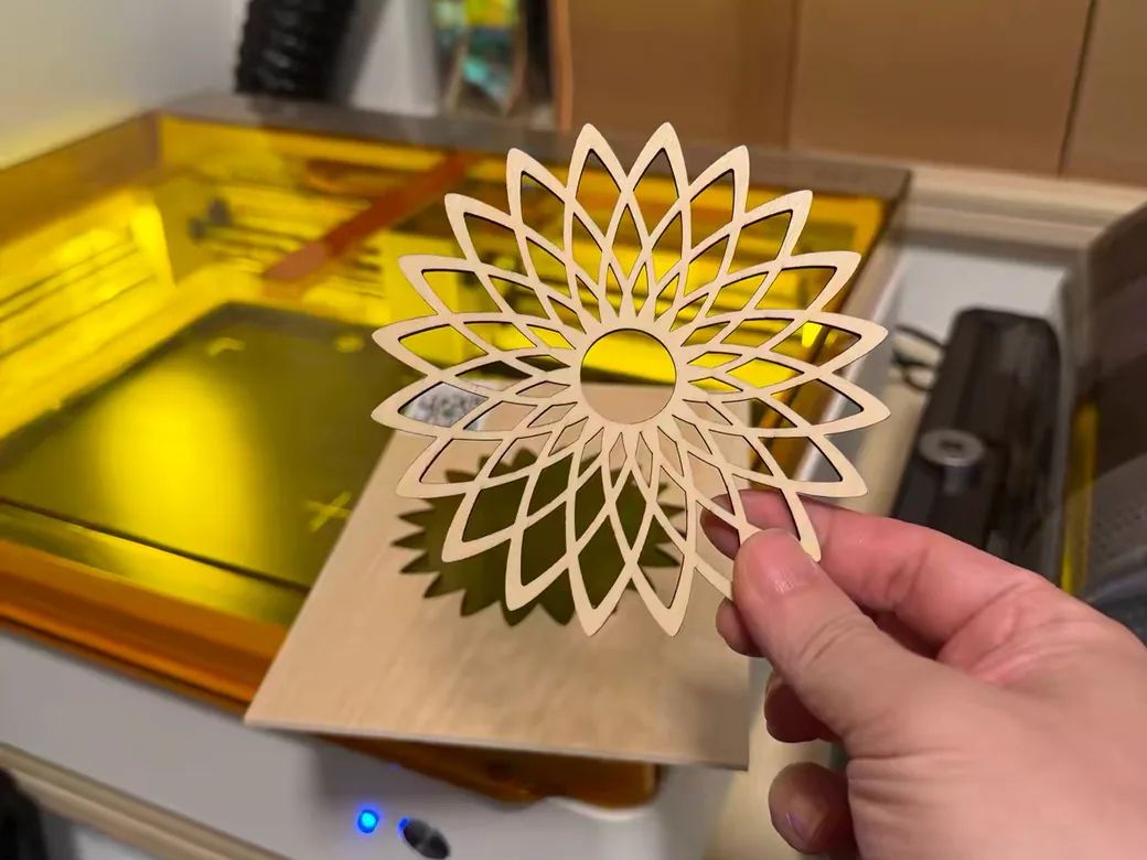 Hand holding a laser-cut wooden mandala in front of an open xTool M2 laser